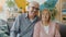 Elderly husband and wife looking at camera with serious faces then smiling and laughing