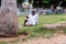An elderly Indian man wearing a white shirt sitting alone on the grass of a green