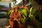 Elderly Indian rural female farmer smiles sitting in orchard planting flowers in pots. Senior Sri Lankan happy woman in