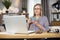 Elderly lady drinking tea while studying report on laptop