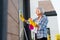 Elderly lady wearing bright yellow gloves feeling busy washing windows