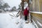 Elderly lone woman cleans the snow near home.