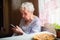 Elderly lone woman sits with a smartphone in her hands.