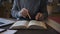 Elderly male biologist professor is examining book sitting at table in university library.