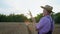 Elderly male farmer in straw hat checks ears of wheat in his hands during harvest in field