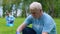 Elderly male volunteer collecting trash in park, smiling to camera, altruism