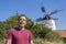 An elderly man with a beard against a background of a windmill and a summer rural landscape.