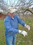 The elderly man cuts apple-tree branches with secateurs. Spring works in a garden