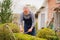 elderly man cuts bushes in the garden with large pruner.