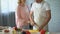 Elderly man cutting fresh salad, loving wife hugging husband, family care