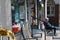 An Elderly Man with Dementia Sits Alone, Lost and Abandoned on a Bench in Front of a Storefront