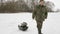 An elderly man enters a frozen lake in the winter and takes things on a sled. A man wearing warm clothes in khaki