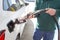 Elderly man with gas hose in hand to fill tank of his green car