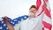 An elderly man with a gray beard holding a US flag on his shoulders. Patriotic day. A man in a cap celebrates US