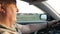 An elderly man with gray hair drives a car with his hands on a black leather steering wheel looking at the road ahead