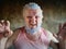 An elderly man with hair, eyebrows and beard covered in blue hair bleaching paint poses for camera showing threatening grimaces