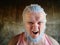 An elderly man with hair, eyebrows and beard covered in blue hair bleaching paint poses for camera showing threatening grimaces