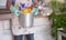 An elderly man holds up a plastic bucket with household cleaning items inside. Only one person with green gloves