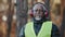 Elderly man professional forestry engineer in protective soundproof headphones standing in forest looking at camera