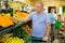 Elderly man purchaser taking fresh tangerines in grocery store