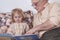 An elderly man reading a book to his grandson. The kid listens carefully