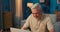 Elderly man sitting at desk with laptop in the evening. Senior works in a salon.