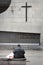 Elderly man sitting in front a crucifix on the church wall