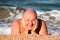 elderly man squints from the sun lying on the sand in the sea foam and basking in the waves