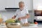 Elderly man standing at kitchen counter with colorful fresh vegetables, fruits and food ingredients, senior man preparing for