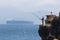 An elderly man is standing on a rock fishing in the Strait of Gibraltar. A container ship drives in the background.