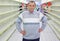 Elderly man stands between empty shelves in shop