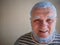 An elderly man in a striped t shirt with blue dye to bleach the hair on his head and beard poses for the camera