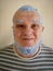 An elderly man in a striped t shirt with blue dye to bleach the hair on his head and beard poses for the camera