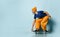 Elderly man in t-shirt, orange pants, hat, gumshoes. Riding black skateboard, posing sideways on blue background. Full length