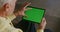 An elderly man uses a tablet, scrolling the screen with a green screen