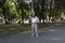 An elderly man walks alone in the park in the summer. A modern retired businessman in a white shirt and trousers is