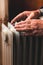 An elderly man warms his hands over an electric heater. In the off-season, central heating is delayed, so people have to buy