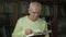 Elderly man wearing eyeglasses reads Bible with bookmark in hand.