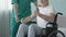 Elderly man in wheelchair lifting dumbbells, nurse by his side helping, trauma