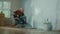 An elderly man in a wheelchair paints a wall with white paint using a long roller. A disabled man in the age makes