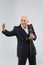 An elderly man on a white background, in a black smart suit calls someone with a rose in his hand