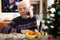 Elderly man wishes Merry Christmas by phone to friends and acquaintances sitting at the festive table in house