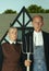 Elderly man and woman in art performance, replica of painting american gothic. Retro style, comparison of eras and