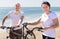 Elderly man with a woman walking with bicycles on the sand