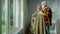 An elderly man wraps plaid around an older woman with cup of tea in his hands. Aged couple of pensioners communicate and