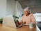 Elderly multi-ethnic female smiling while scrolling on her laptop in her modern home.