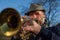 An elderly musician plays in the street on a trumpet