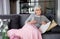 Elderly pensive lady relaxing on couch with book