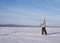 Elderly person alone doing Nordic walking in winter sunny day on a snow-covered lake, outdoor, side view.