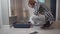 Elderly pet owner prepares indoor cat litter box with Scottish Straight cat at home. Senior female and gray british cat